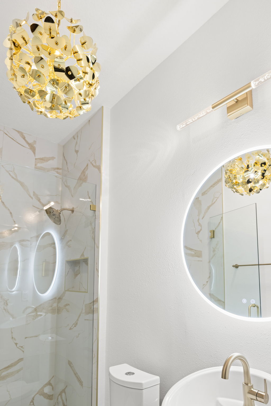 Luxurious bathroom with gold light fixture and mirror.
